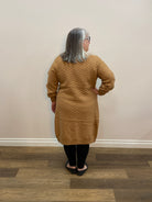 Person wearing a brown sweater standing against a white wall.