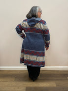 Person wearing a patterned sweater standing against a plain wall.