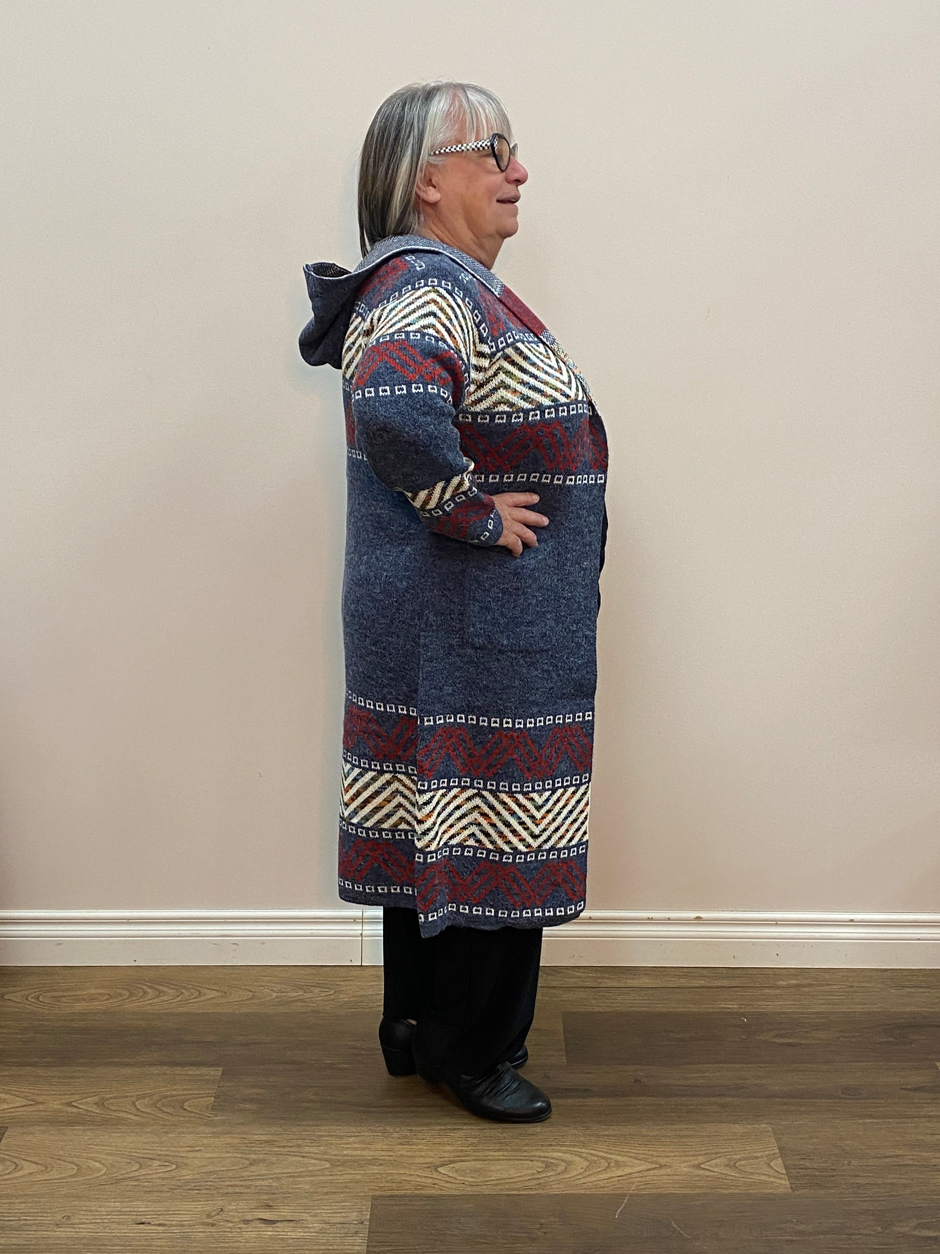 Person wearing a patterned coat standing against a plain wall.