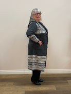 Person wearing a dark gray coat with white patterned sleeves standing against a plain wall.