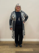 Person wearing a black outfit with geometric patterns in a room with wooden flooring and a white wall.