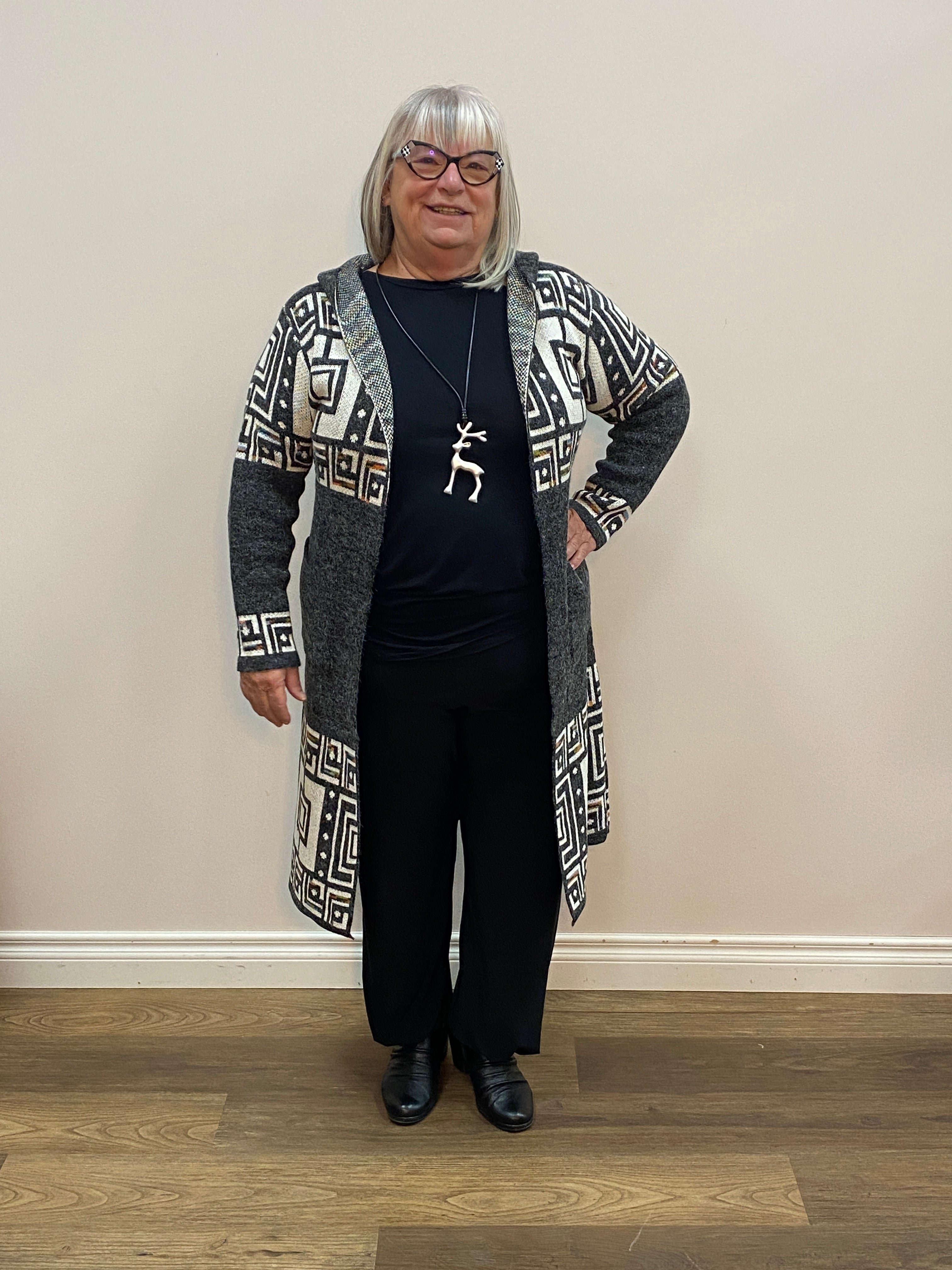 Person wearing a black outfit with geometric patterns in a room with wooden flooring and a white wall.