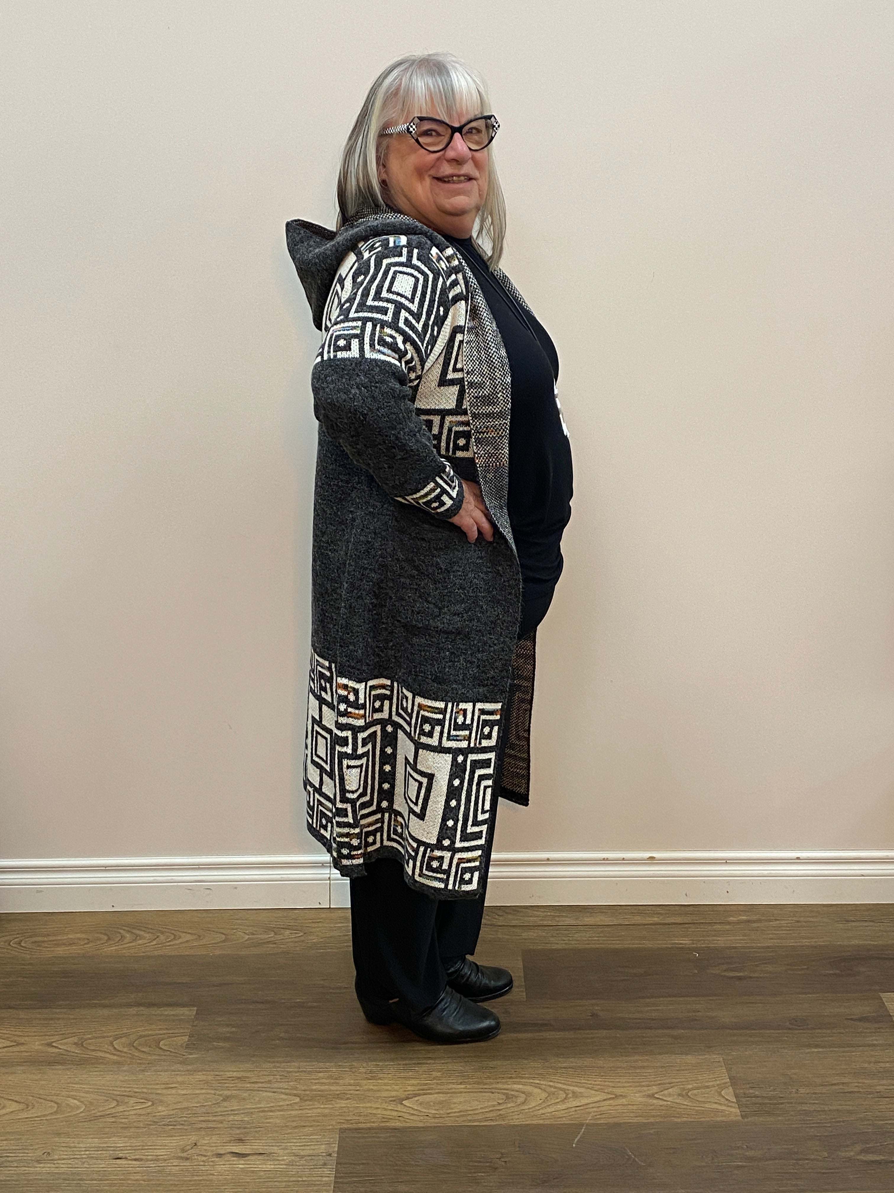 Person wearing a dark coat with a patterned interior standing against a plain wall.