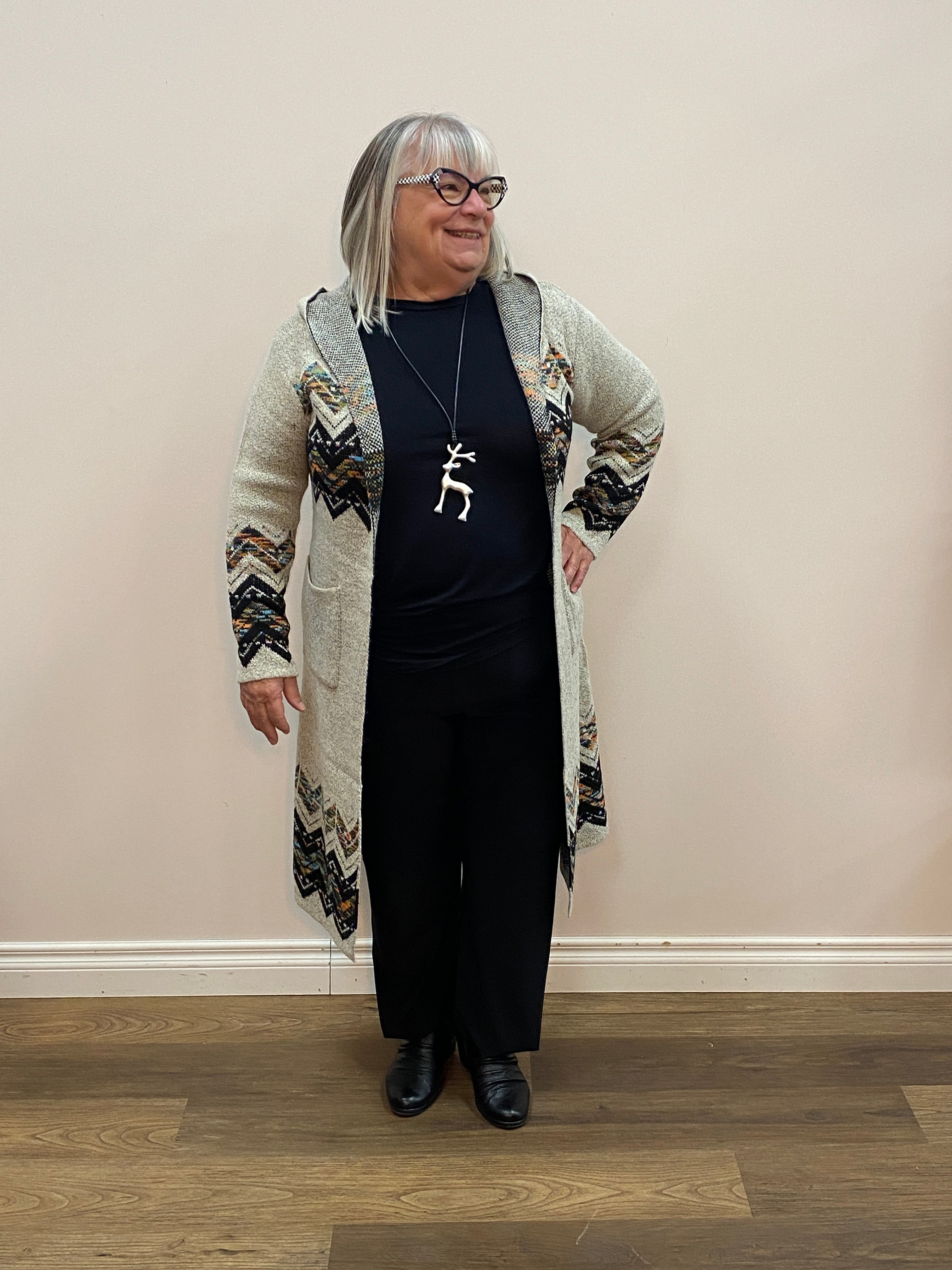 Person wearing a black outfit with a patterned sweater in a room with wooden flooring.