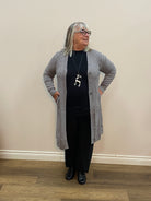 Person wearing a gray cardigan, black top, and black pants in a room with a wooden floor and white walls.