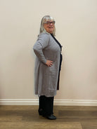 Person wearing a gray sweater and black pants standing against a beige wall.