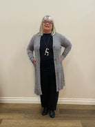 Person wearing a gray cardigan, black top, and black pants in a room with beige walls and wooden flooring.