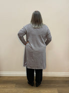 Person wearing a gray sweater standing in a room with a wooden floor and beige wall.