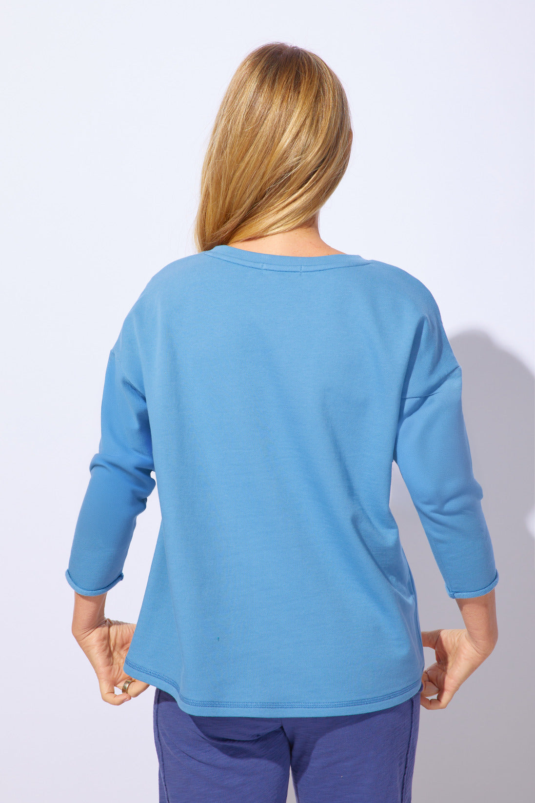 Person wearing a blue long-sleeve top and pants on a light purple background