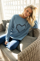 Woman wearing a light blue sweater with a heart design, sitting on a couch.