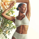 LIfestyle image of the Beyond Bra in Aloe on a model with flowers in the background. 
