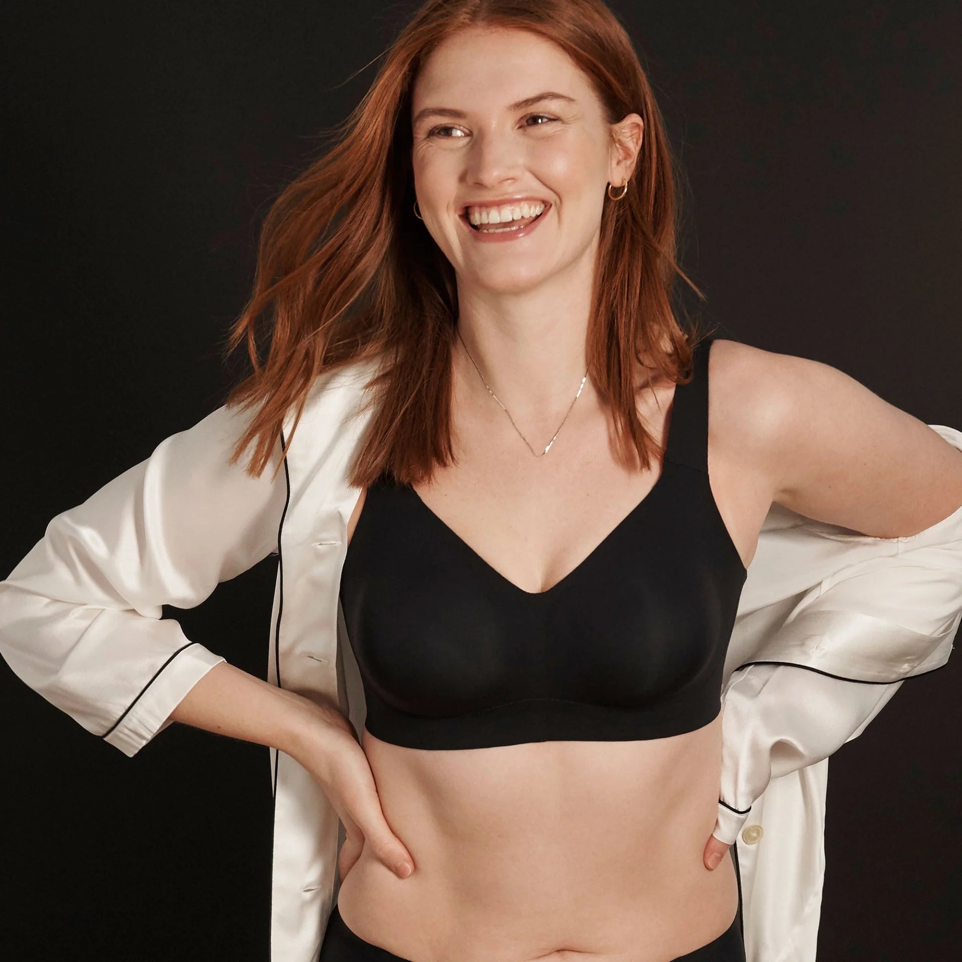 The Beyond Bra in Black shown on a model who is smiling and wearing a satin pj shirt over her arms. 