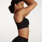 Woman wearing the Evelyn & Bobbie Defy Bra in Black, no wire pullover bra, against a white background, side view. 