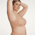 Woman wearing the Evelyn & Bobbie Defy bra in Himalayan Salt, light pinkish beige no wire pullover bra, against a white background, side view. 