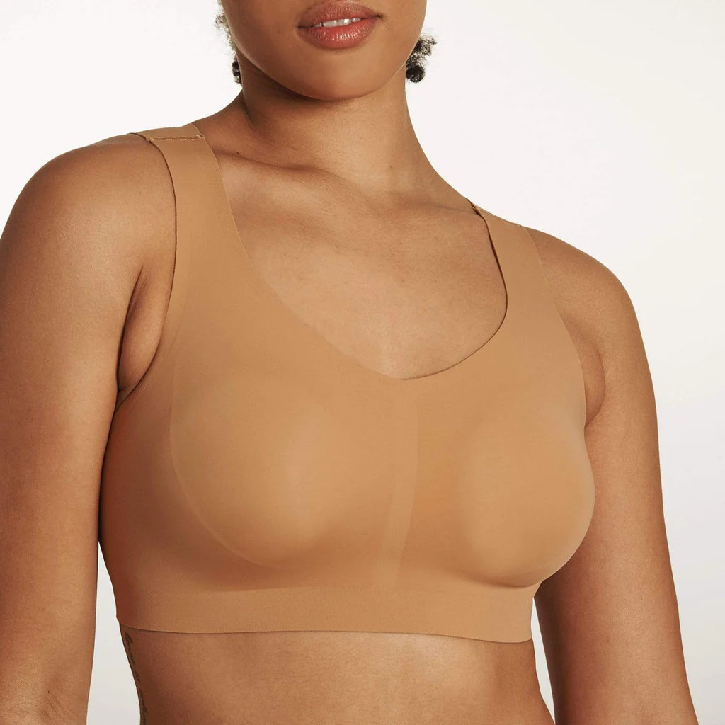 Close up of Woman wearing the Evelyn & Bobbie Defy Bra in Mica, light tan no wire pullover bra, against a white background. 