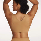 Woman wearing the Evelyn & Bobbie Defy Bra in Mica, light tan no wire pullover bra, against a white background, back view. 