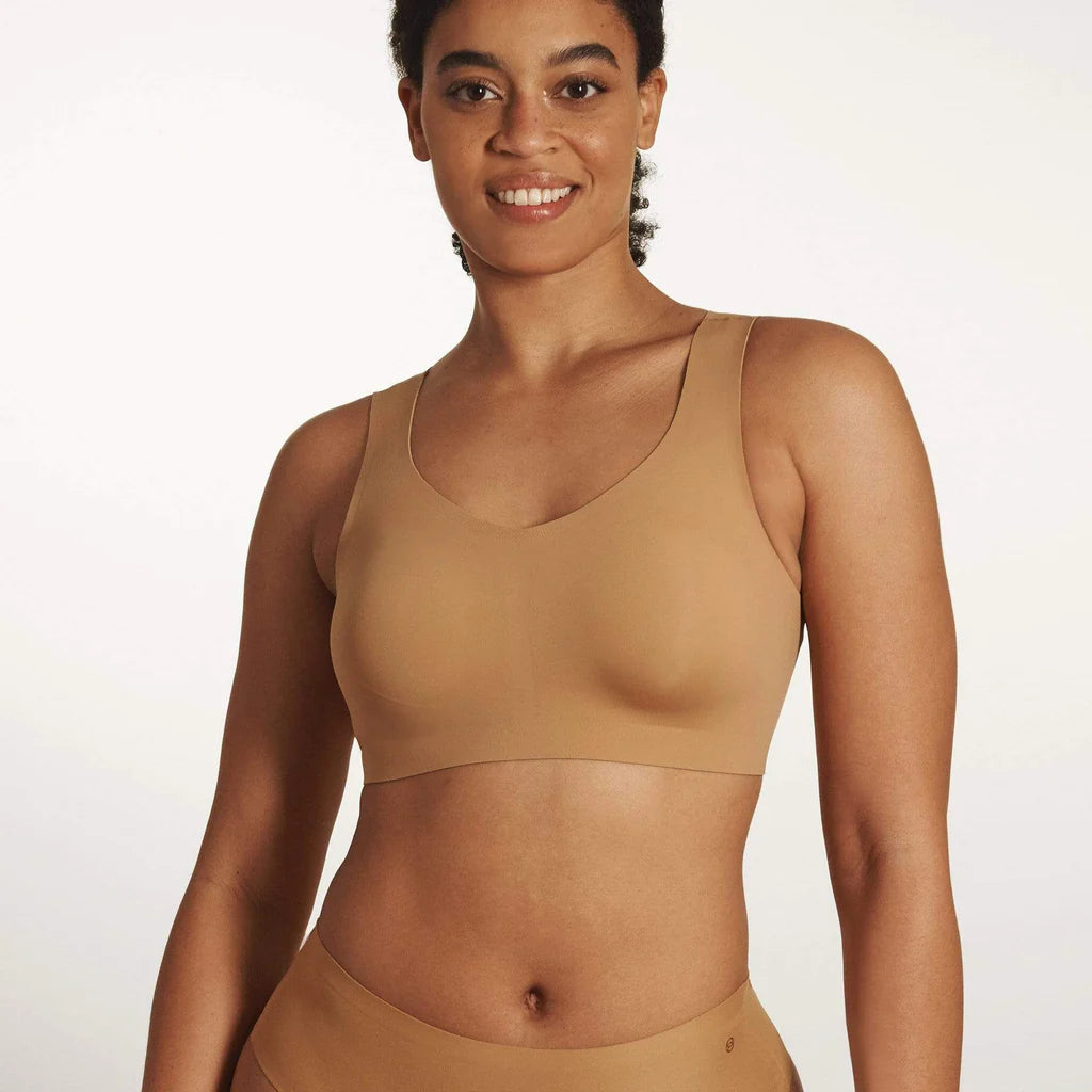 Woman wearing the Evelyn & Bobbie Defy Bra in Mica, light tan no wire pullover bra, against a white background. 