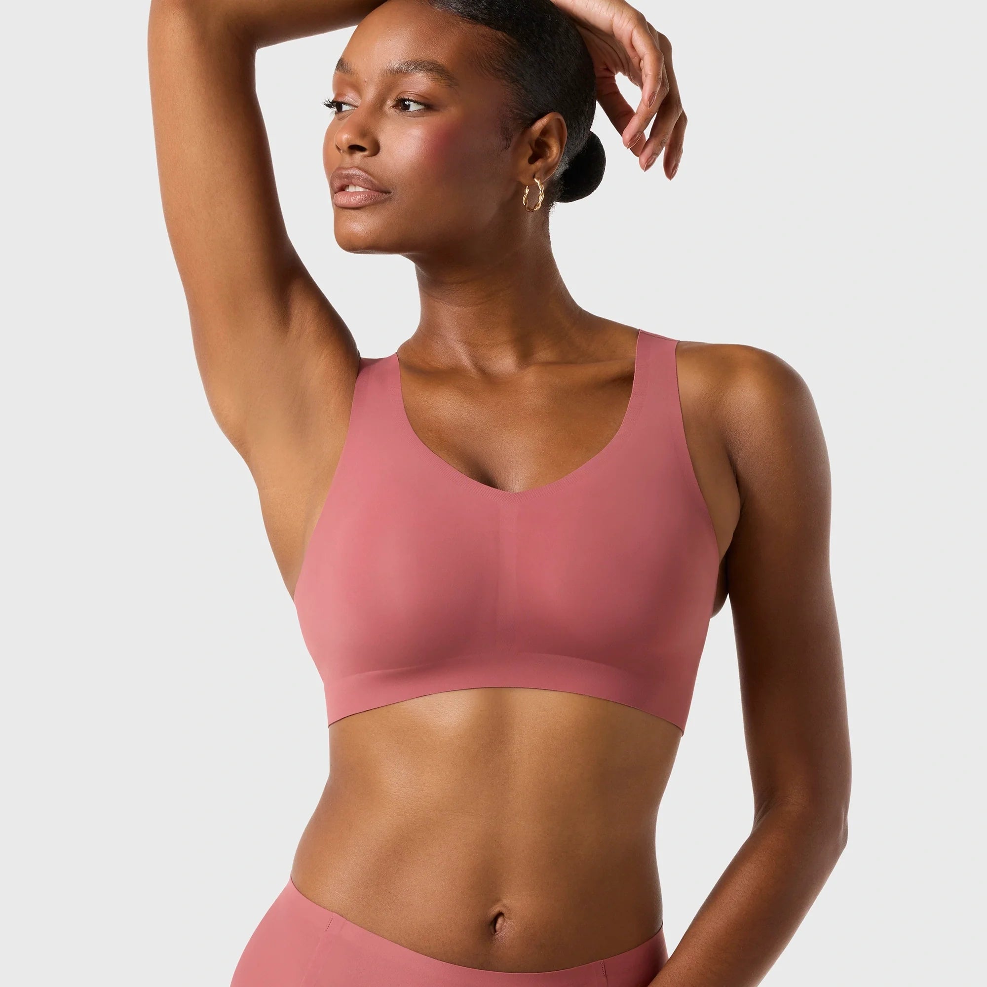 Woman wearing the Evelyn & Bobbie Defy Bra in Pink Canyon, soft pink no wire pullover bra, on a white background. 
