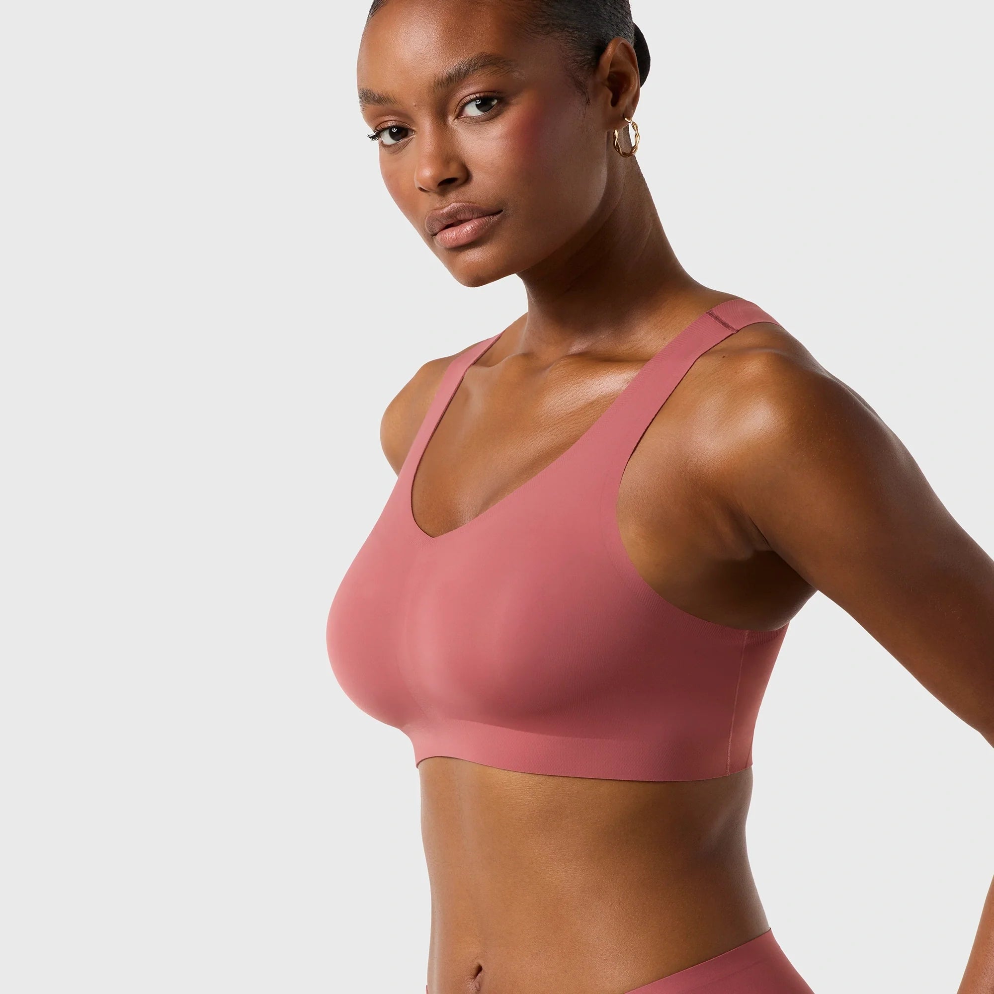 Woman wearing the Evelyn & Bobbie Defy Bra in Pink Canyon, soft pink no wire pullover bra, on a white background. 