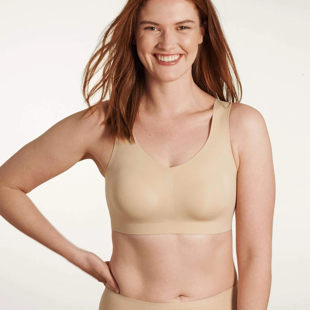 A woman wearing the Evelyn & Bobbie Defy Bra in Sand, light beige no wire bra, on a white background. 