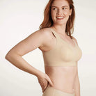A woman wearing the Evelyn & Bobbie Defy Bra in Sand, light beige no wire bra, on a white background. 
