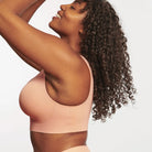 Woman wearing Evelyn & Bobbie Evelyn Bra in Himalayan Salt, light pink no wire pullover bra, against a white background, side view. 