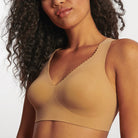 Woman wearing the Evelyn & Bobbie Evelyn Bra in Mica, tan no wire pullover bra, against a white background, close up front view. 