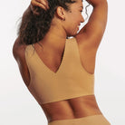 Woman wearing the Evelyn & Bobbie Evelyn Bra in Mica, tan no wire pullover bra, against a white background, back view. 