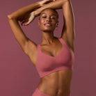 Woman wearing the Evelyn & Bobbie Evelyn Bra in Pink Canyon, dusty pink no wire pullover bra, on a pink background, front view. 
