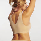 Woman wearing the Evelyn & Bobbie Evelyn Bra in Sand, beige no wire pullover bra with scalloped edges, on a white background, back view. 