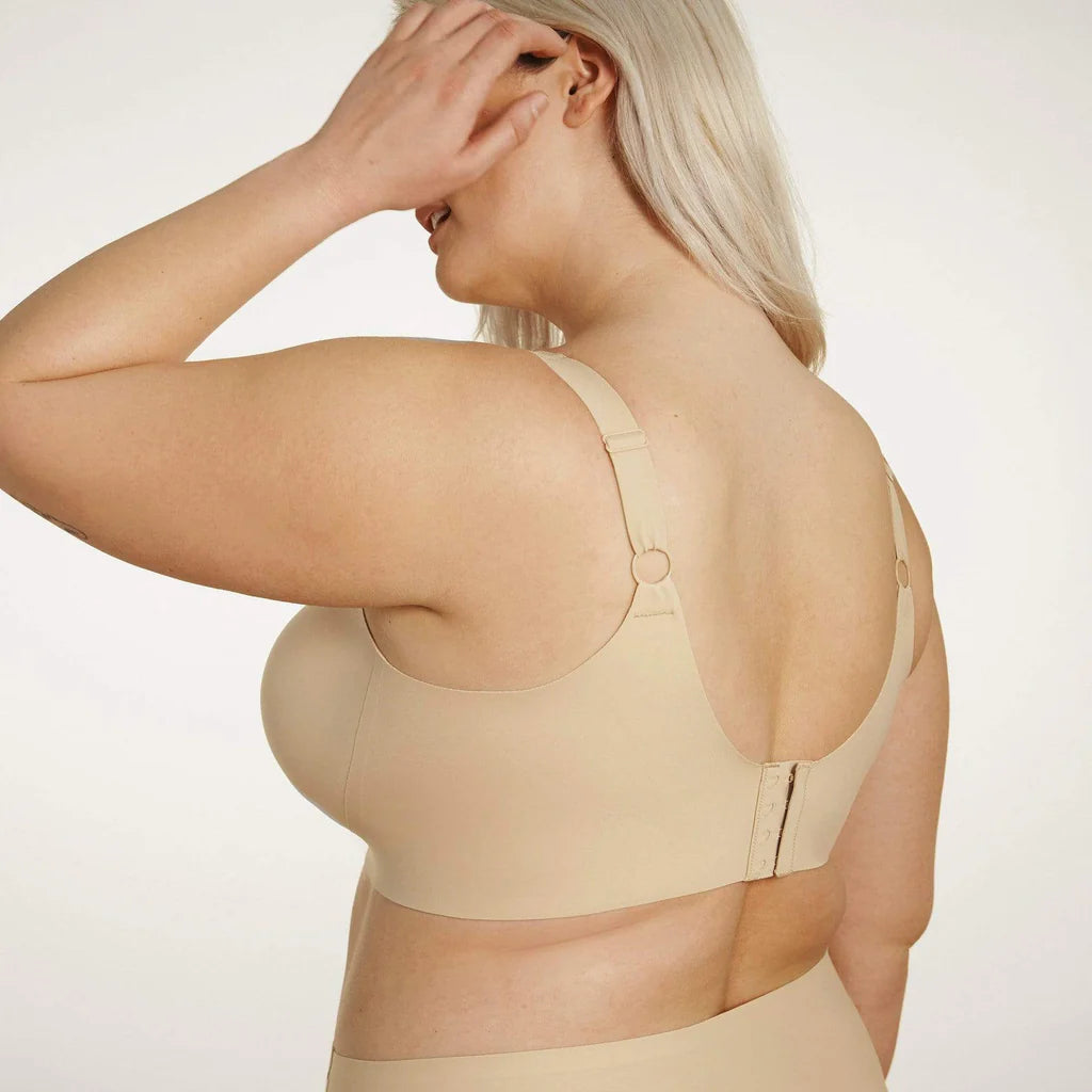 Beyond Bra in Sand, a beige wirefree bra shown on a model from a back view so you can see the side and back band. 