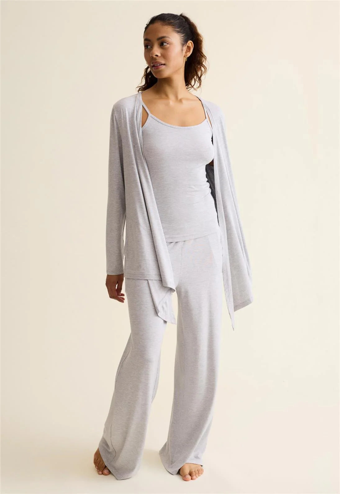 Woman wearing a light gray outfit with a matching cardigan on a plain background