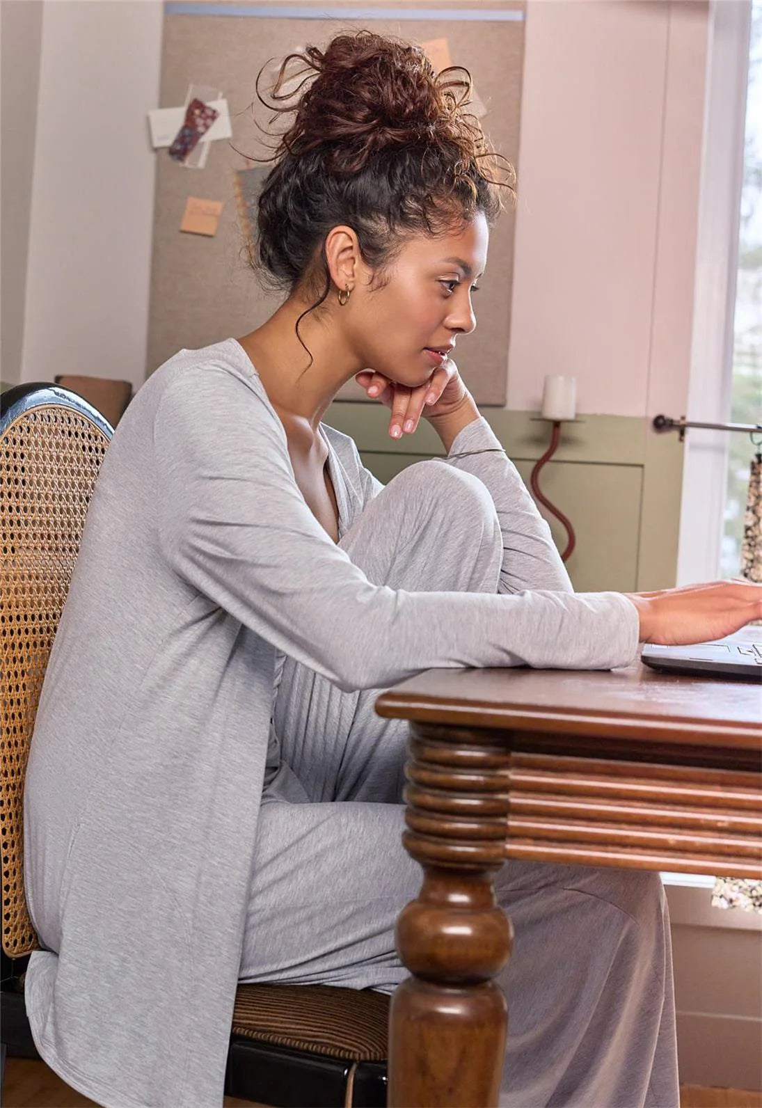 Woman sitting at a wooden table in a home setting, looking thoughtful.