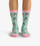 Green socks with pink accents and owl pattern worn by a person on a white background