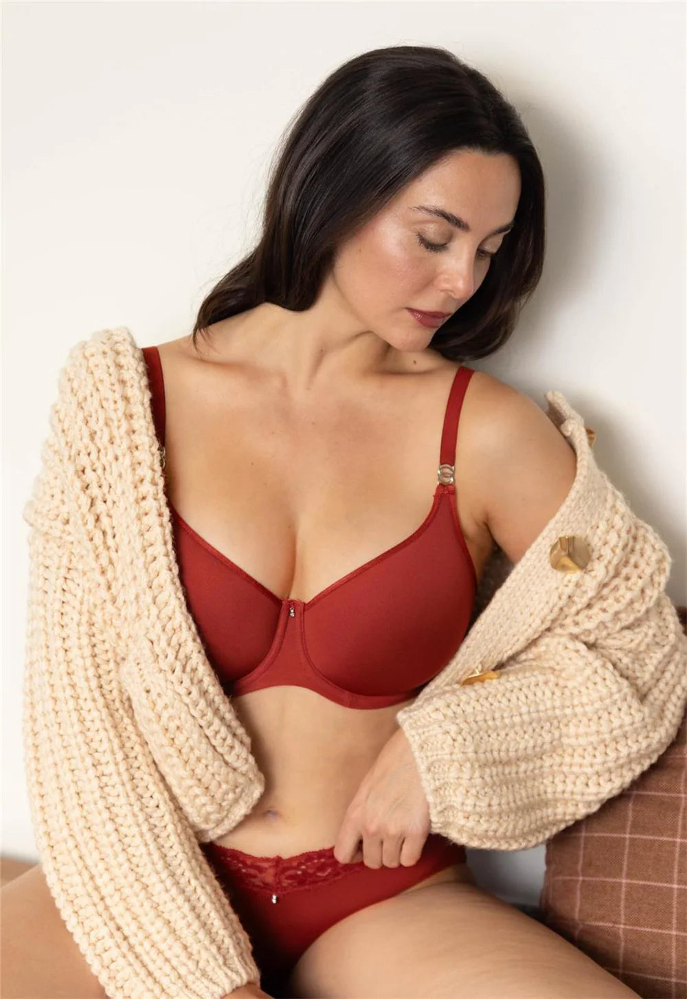 Woman wearing a red bra and panties with a beige cardigan.