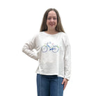 Person wearing a white long-sleeve Papa Bicycle Pullover shirt and blue jeans standing on a white background. 