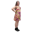 Woman wearing a colorful floral Papa Classic Print dress in Pink against a plain wall, side view. 