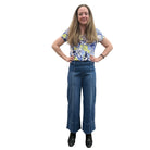 Person wearing a blue floral top and blue Papa Comfort Crop jeans standing against a plain wall, front view. 