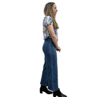 Person wearing a blue floral top and blue Papa Comfort Crop jeans standing against a plain wall, side view. 