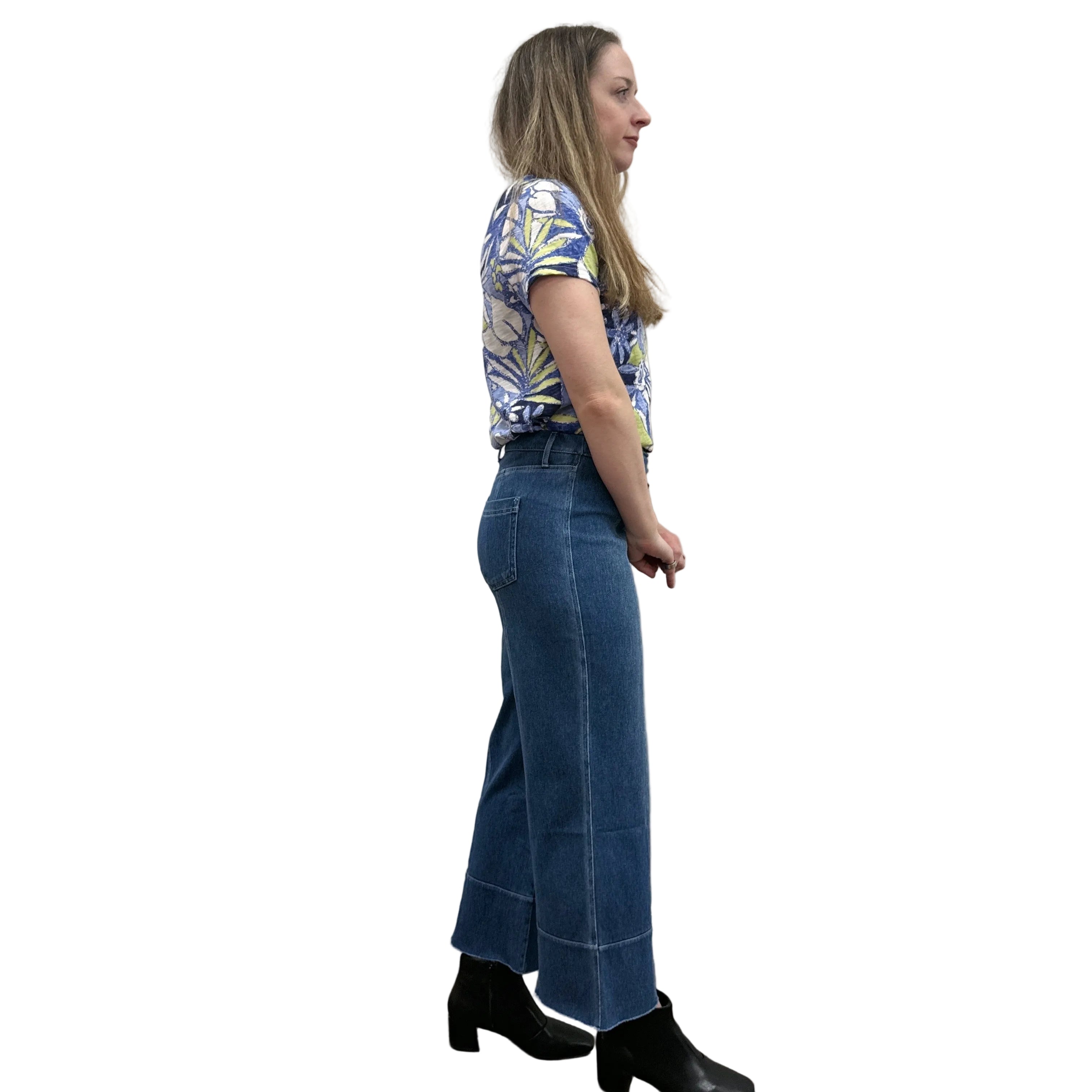 Person wearing a blue floral top and blue Papa Comfort Crop jeans standing against a plain wall, side view. 