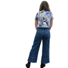 Person wearing a blue floral top and blue Papa Comfort Crop jeans standing against a plain wall, back view. 