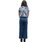 Person wearing a blue floral top and blue Papa Comfort Crop jeans standing against a plain wall, back view. 