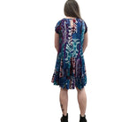 Woman wearing the Papa Indigo Mosaic Breeze patterned dress against a white background, facing the wall to see the back view of the dress. 