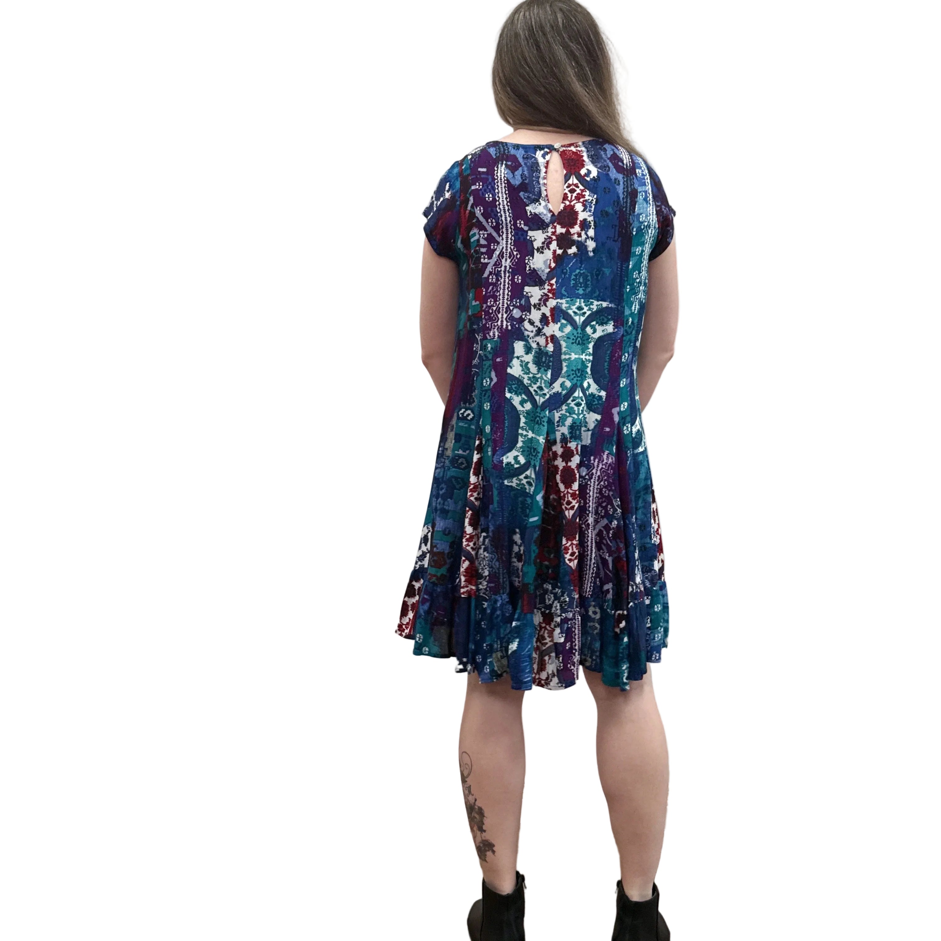 Woman wearing the Papa Indigo Mosaic Breeze patterned dress against a white background, facing the wall to see the back view of the dress. 