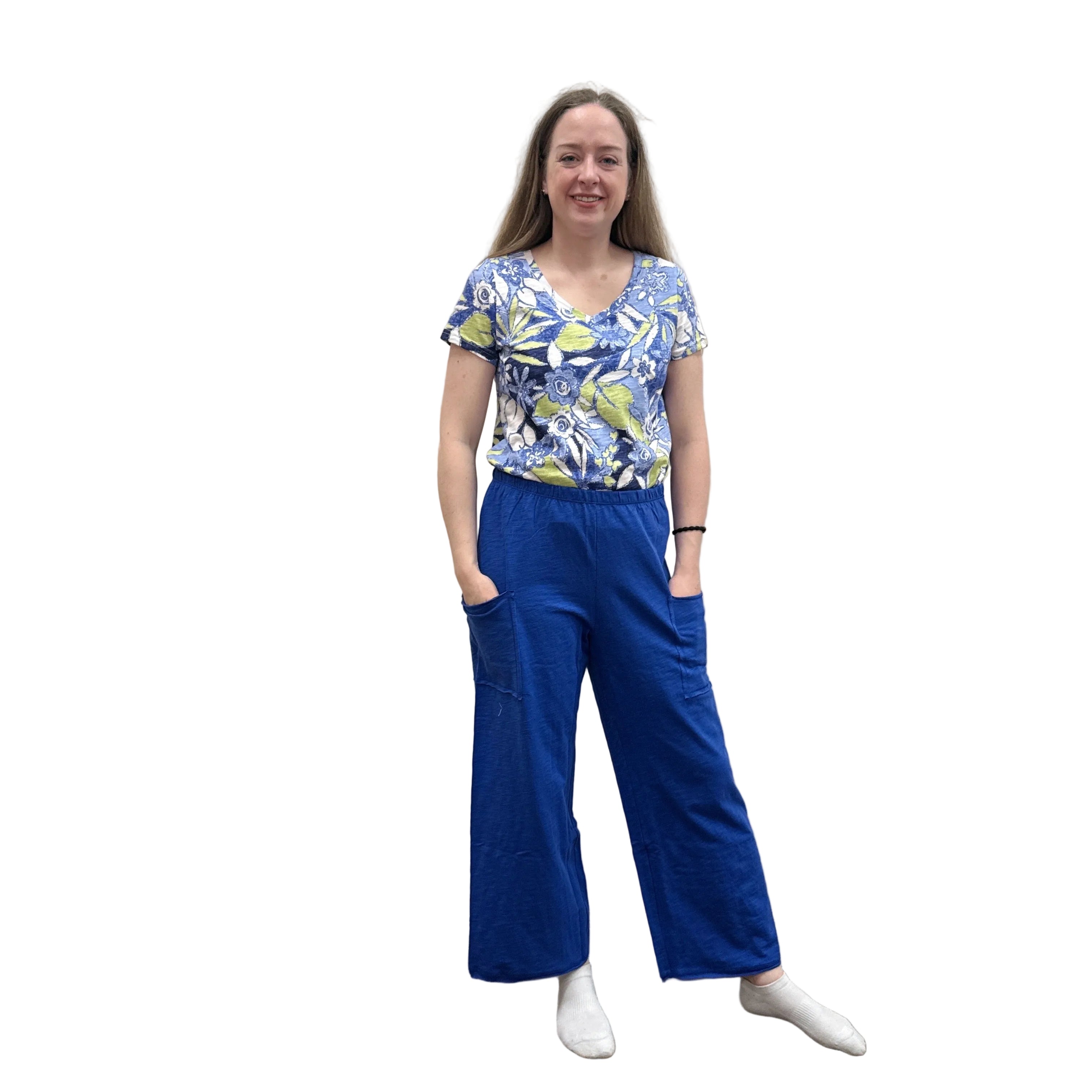 Woman wearing a blue floral top and blue Papa Pocket Flood pants standing against a plain wall.