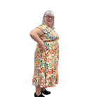 Woman wearing a colorful patterned Papa Saffron Bloom Midi dress against a plain wall side view.