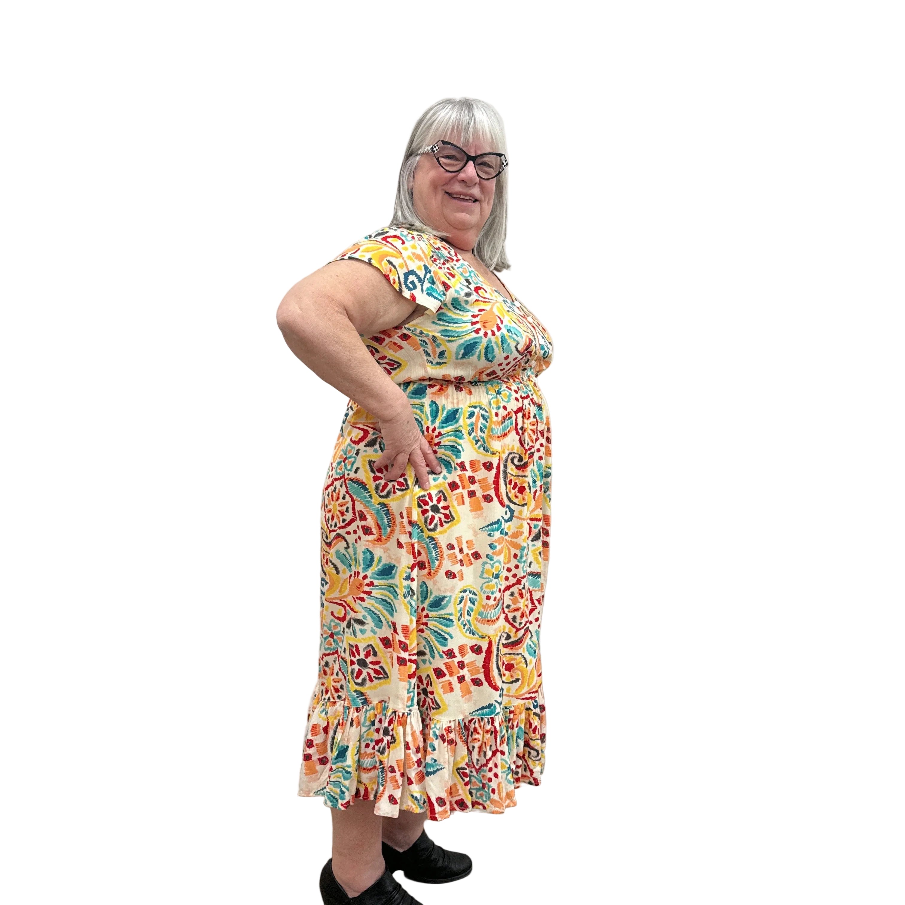 Woman wearing a colorful patterned Papa Saffron Bloom Midi dress against a plain wall side view.