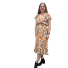 Woman wearing a colorful patterned Papa Saffron Bloom Midi dress against a plain wall.