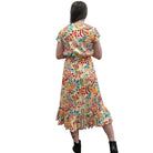 Woman wearing a colorful patterned Papa Saffron Bloom Midi dress against a plain wall facing the wall. 