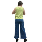 Person wearing a green sleeveless Papa V-Neck Tank top and blue jeans standing against a plain wall.